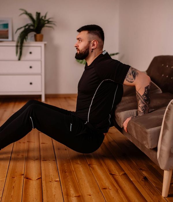 Man performing a controlled bodyweight exercise in a minimalist dark room.